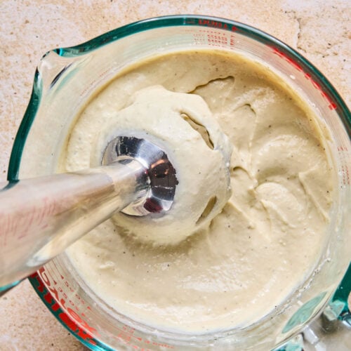 Overhead shot of kale caesar dressing in a measuring cup with an immersion blender in it.