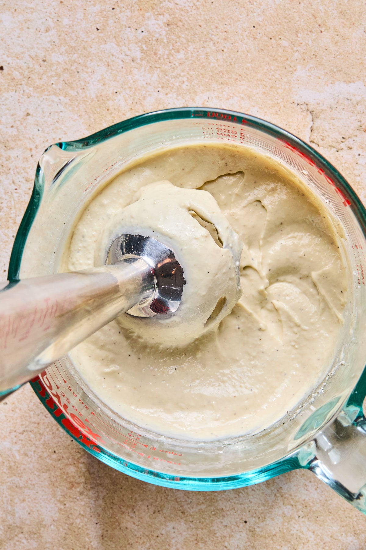Overhead shot of kale caesar dressing in a measuring cup with an immersion blender in it.