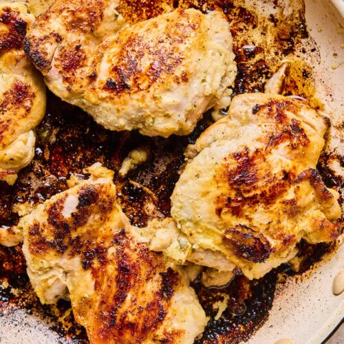 Seasoned cooked chicken thighs in a skillet.