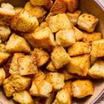 A close up of a bowl of sourdough croutons. Next to the bowl is a tan linen towel.