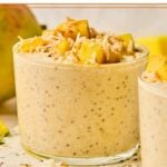 A jar of mango overnight oats topped with fresh diced mango and shredded coconut. Around the jar is another jar of overnight oats and a whole mango.